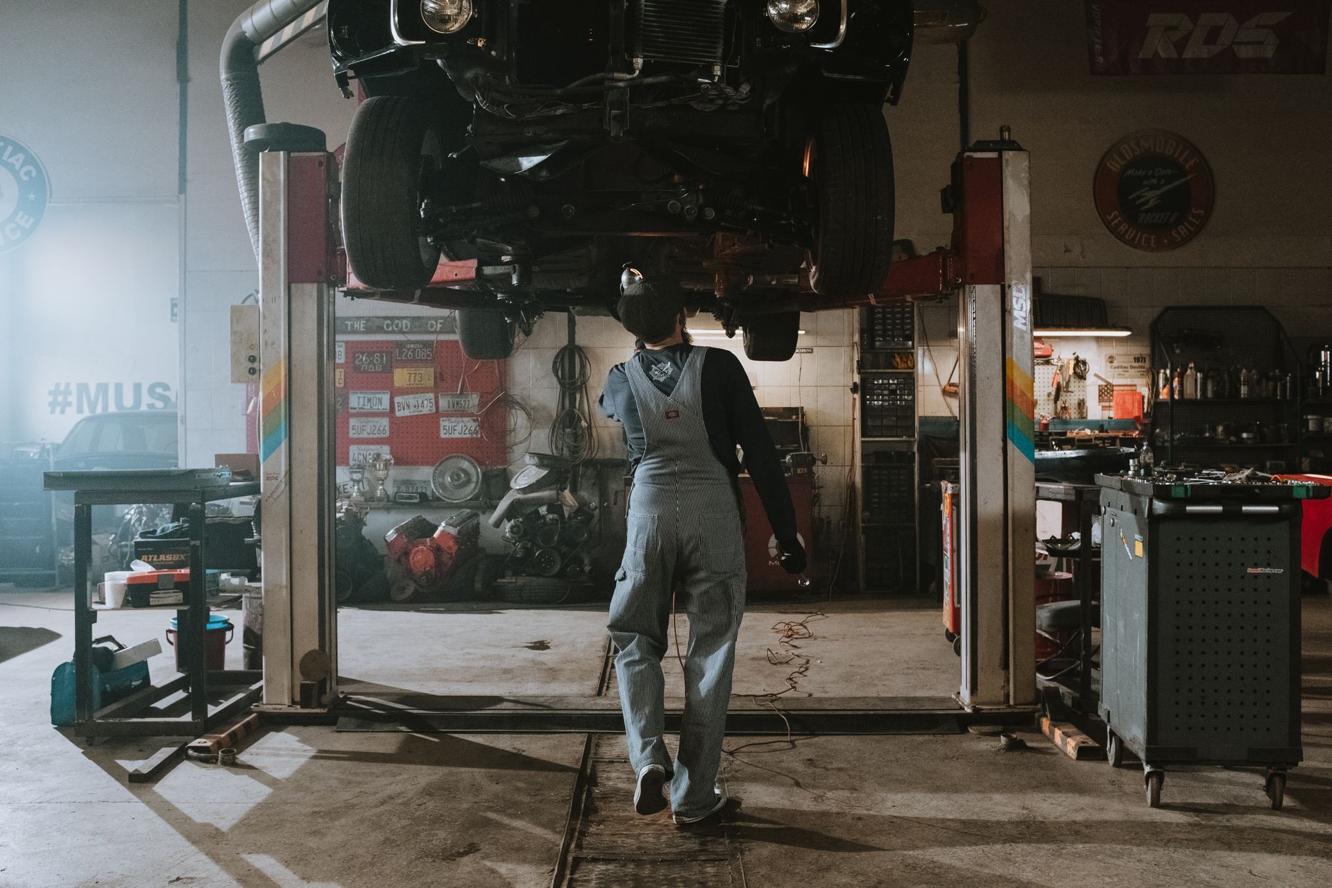 A car raised on a lift inside an auto repair garage while a mechanic works underneath it