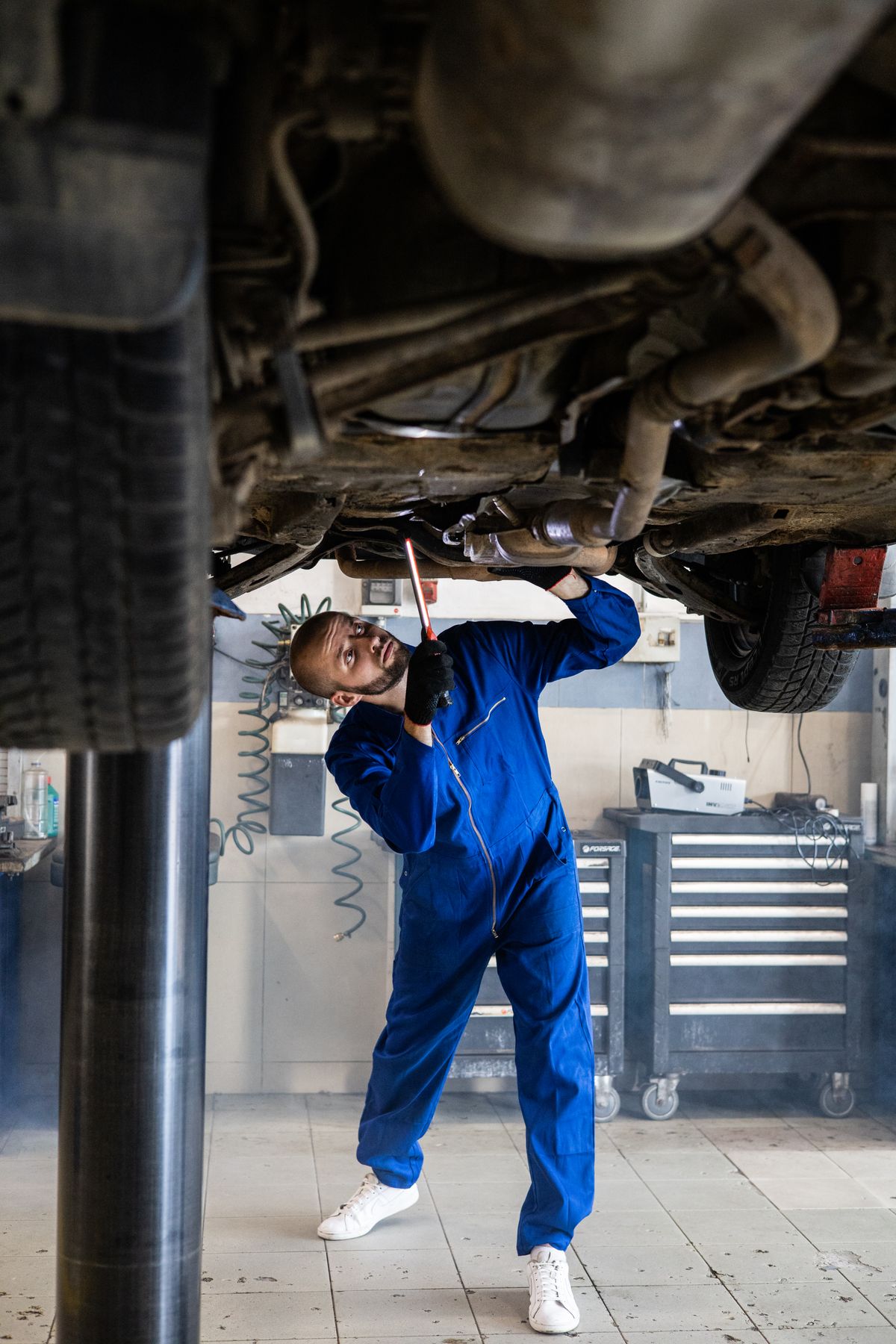 Mechanic in coveralls inspecting the exhaust under a raised car